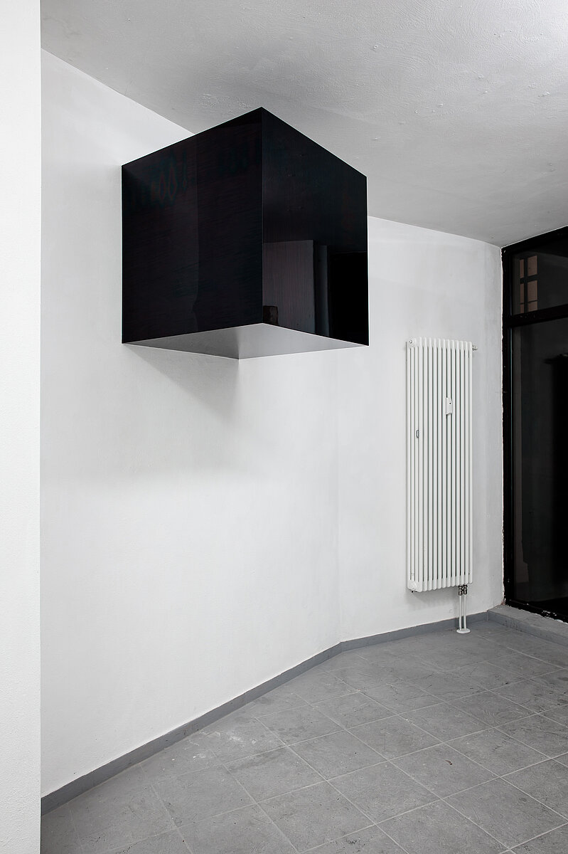 Eine schwarze Glasbox hängt zwei Meter über dem Boden an der Wand.