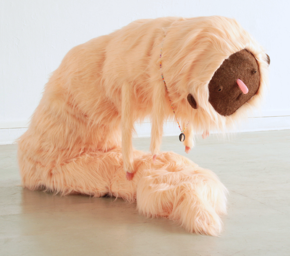 Ein großes braunes, wurmförmiges Stofftier mit einem traurigen Gesicht sitzt auf dem Boden.
