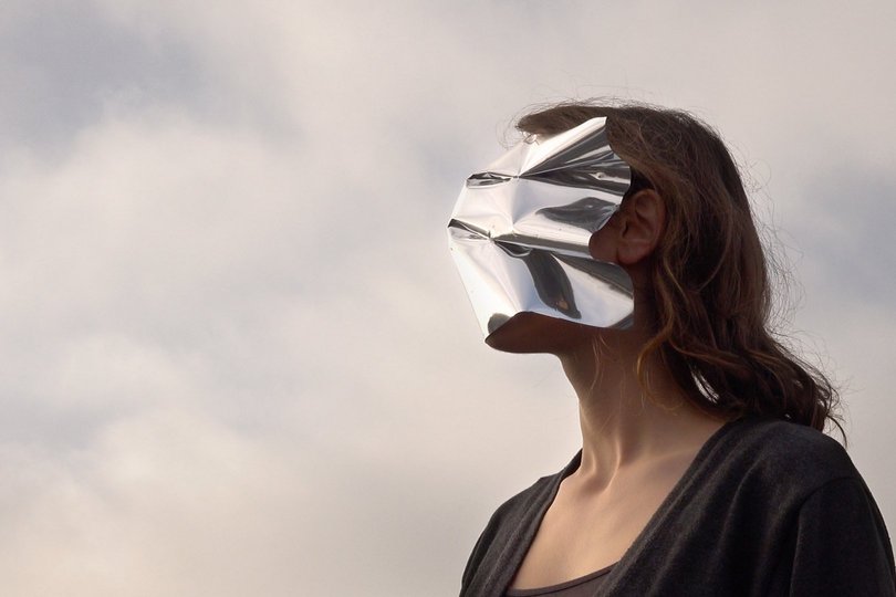  Foto eines Kunstwerkes von Jessica Arseneau: Frau mit silberner Folie vor dem Gesicht, im Hintergrund grauer Himmel