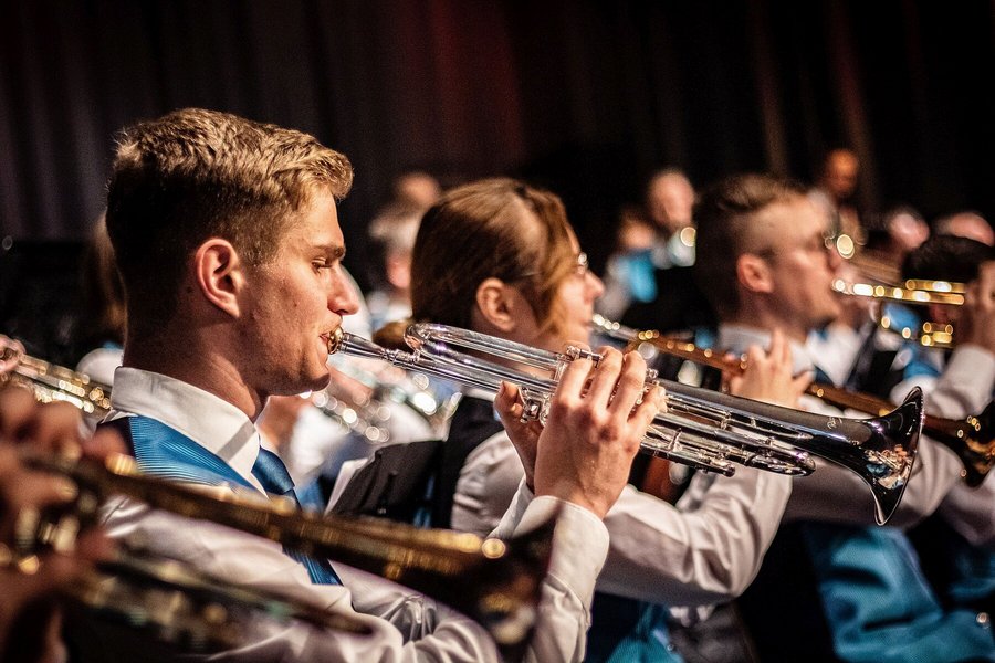 Profilansicht von Trompetern und Trompeterinnen, die gemeinsam in Auftrittskleidung ein Konzert spielen.