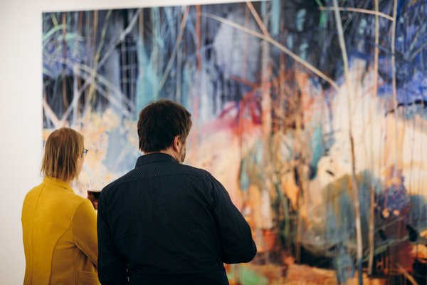 Zwei Personen stehen mit dem Rücken zur Kamera und betrachten ein großflächiges Gemälde. 