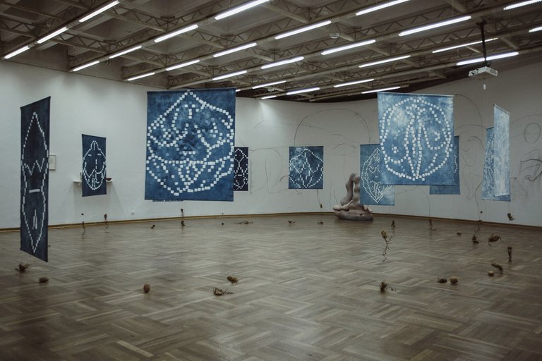 Kunstinstallation aus im Kreis arrangierten blauen Quadraten mit weißen Ornamenten, die mithilfe von Draht über dem Boden schweben. 