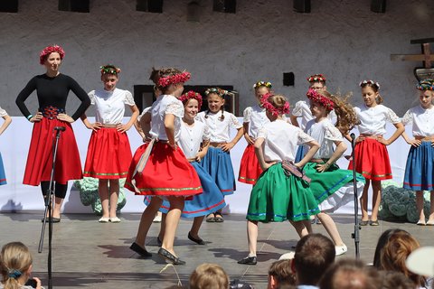 Eine Gruppe Mädchen in Trachten und mit Blumenkränzen auf den Köpfen tanzt auf einer Bühne im Kreis.