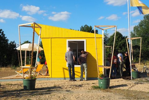 Eine gelbe Hütte umringt von interessierten Besuchern.