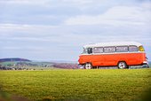Auf einem grünen Hügel steht ein orangenfarbener DDR-Oldtimer-Bus.