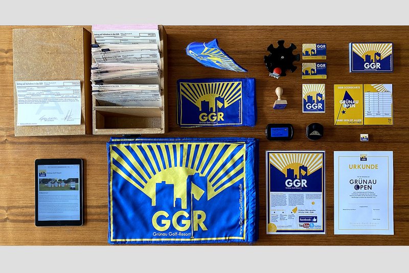 Auf einem Tisch sind verschiedene Wimpel, Urkunden, Stempel, Karteikarten usw. ordentlich nebeneinander aufgereiht. Alle Utensilien sind in blau-gelb gehalten und tragen den Schriftzug GGR. 