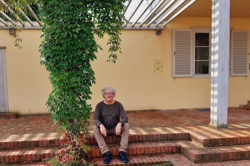Der Übersetzer-Stipendiat Theodor Votsos sitzt auf Terrassenstufen. Neben ihm ist ein Häuserpfosten mit einer Pflanzenranke geschmückt.