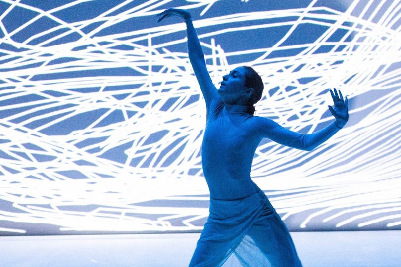 Eine Lichtinstallation in Blau und Weiß, davor tanzt eine Frau.