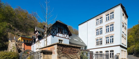 Das Max Uhlig Haus bestehend aus blauem Wohn- und Atelierhaus im Industriestil zwischen einem angrenzenden Wald und einer Straße.  