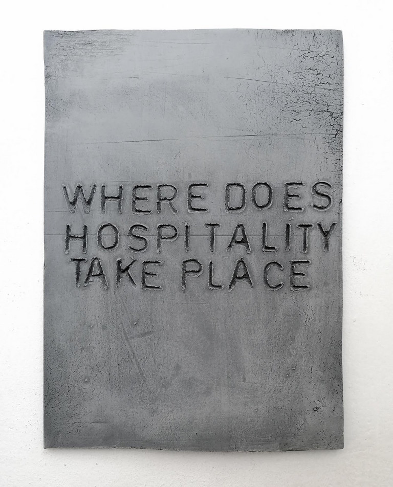 Graues Rechteck aus Ton mit der Gravur "Where Does Hospitality Take Place" in Großbuchstaben.