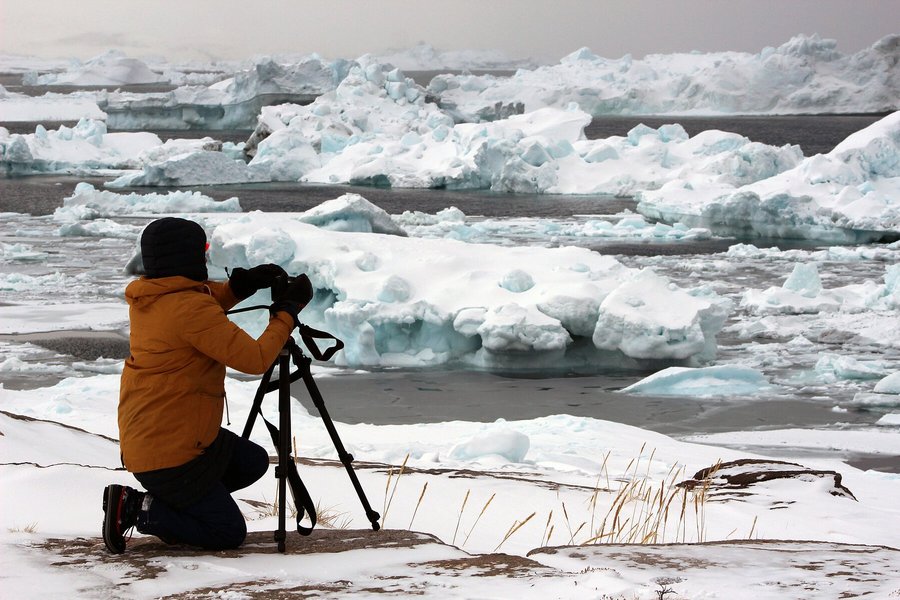Ein Mann hockt in einer Eislandschaft. Er fotografgiert Eisschollen.  