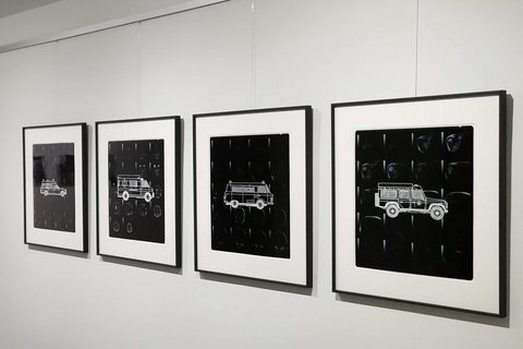 In einem Flur hängen vier Röntgenbilder mit weißen Fahrzeugen an der Wand.  