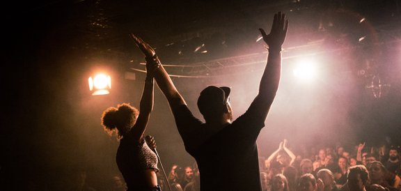 Zwei Menschen auf einer Bühne werden vom Publikum bejubelt.