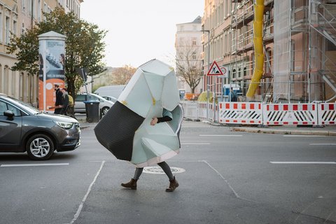 Umhüllt von einer dreidimensionalen Konstruktion, läuft eine Person über eine zweispurige Straße.