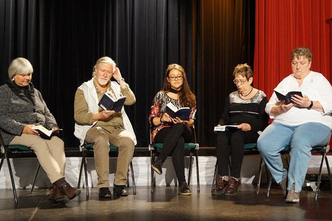 Fünf Menschen sitzen im Halbkreis auf einer Bühne. Alle lesen das gleiche Buch.