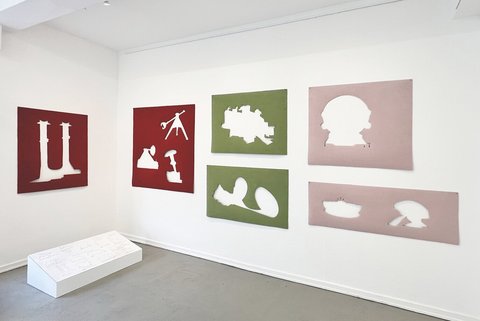In einem weißen Ausstellungsraum hängen mehrere große Scherenschnitte in rot, grün und rosa an der Wand.
