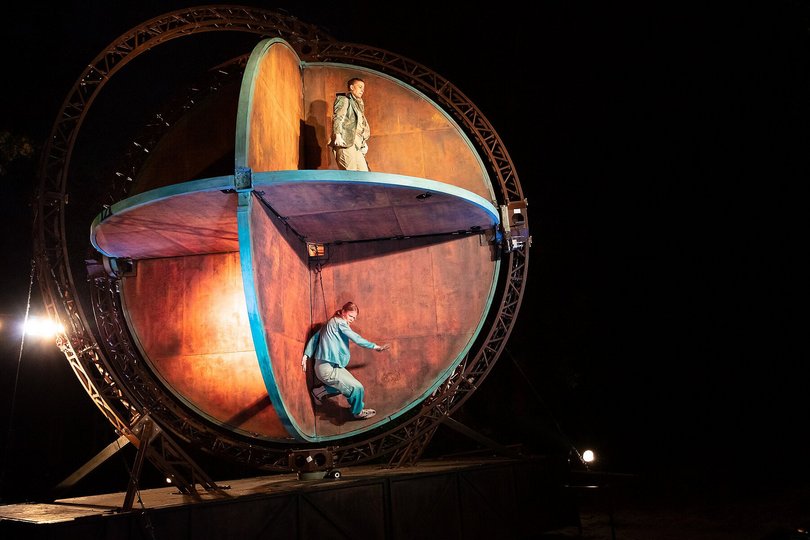 In einer großen globusartigen Holzkonstruktion stehen zwei Performerinnen.