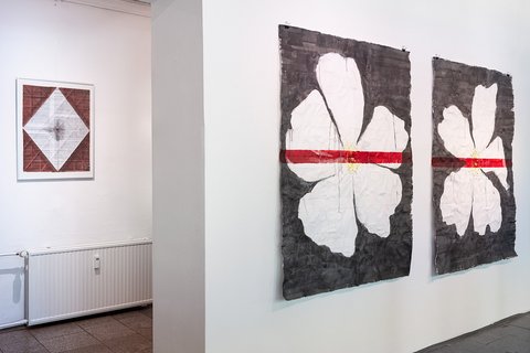 Zwei große Gemälde an einer Ausstellungswand zeigen je eine weiße Blume auf schwarzem Grund, über die ein roter Strich gezogen ist.